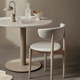 Round marble table with lamp and glassware and chair in a neutral minimalist setting.
