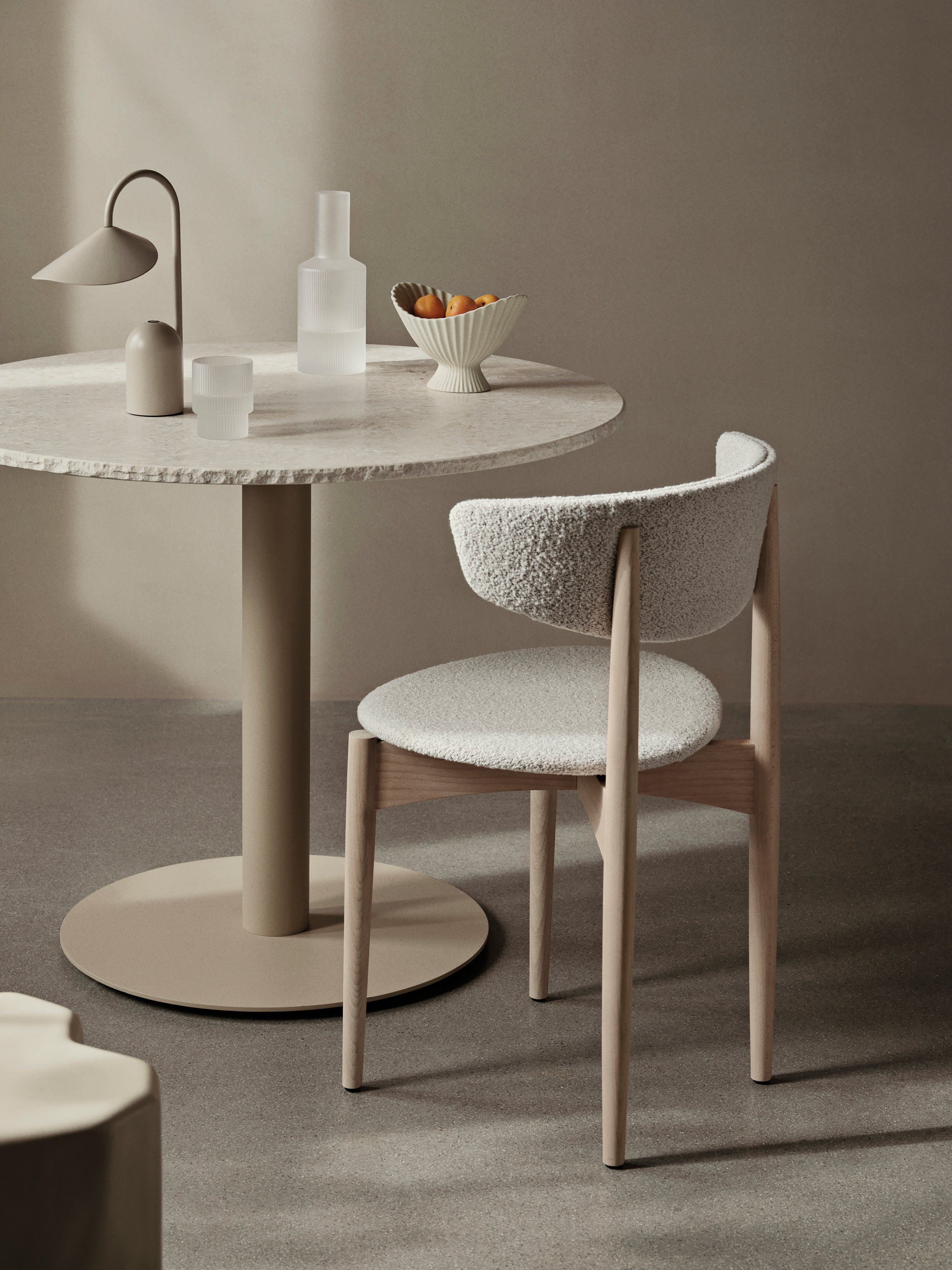 Round marble table with lamp and glassware and chair in a neutral minimalist setting.