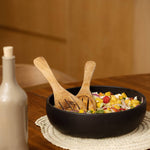 Black bowl with salad on a wooden table next to a bottle