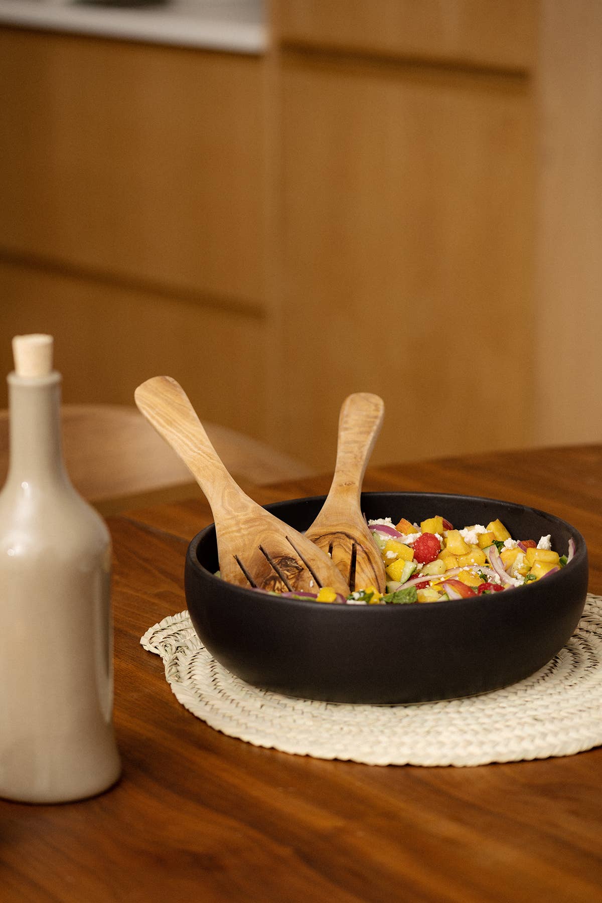 Black bowl with salad on a wooden table next to a bottle