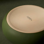 Underside of green ceramic bowl with a visible brand logo on a dark green background