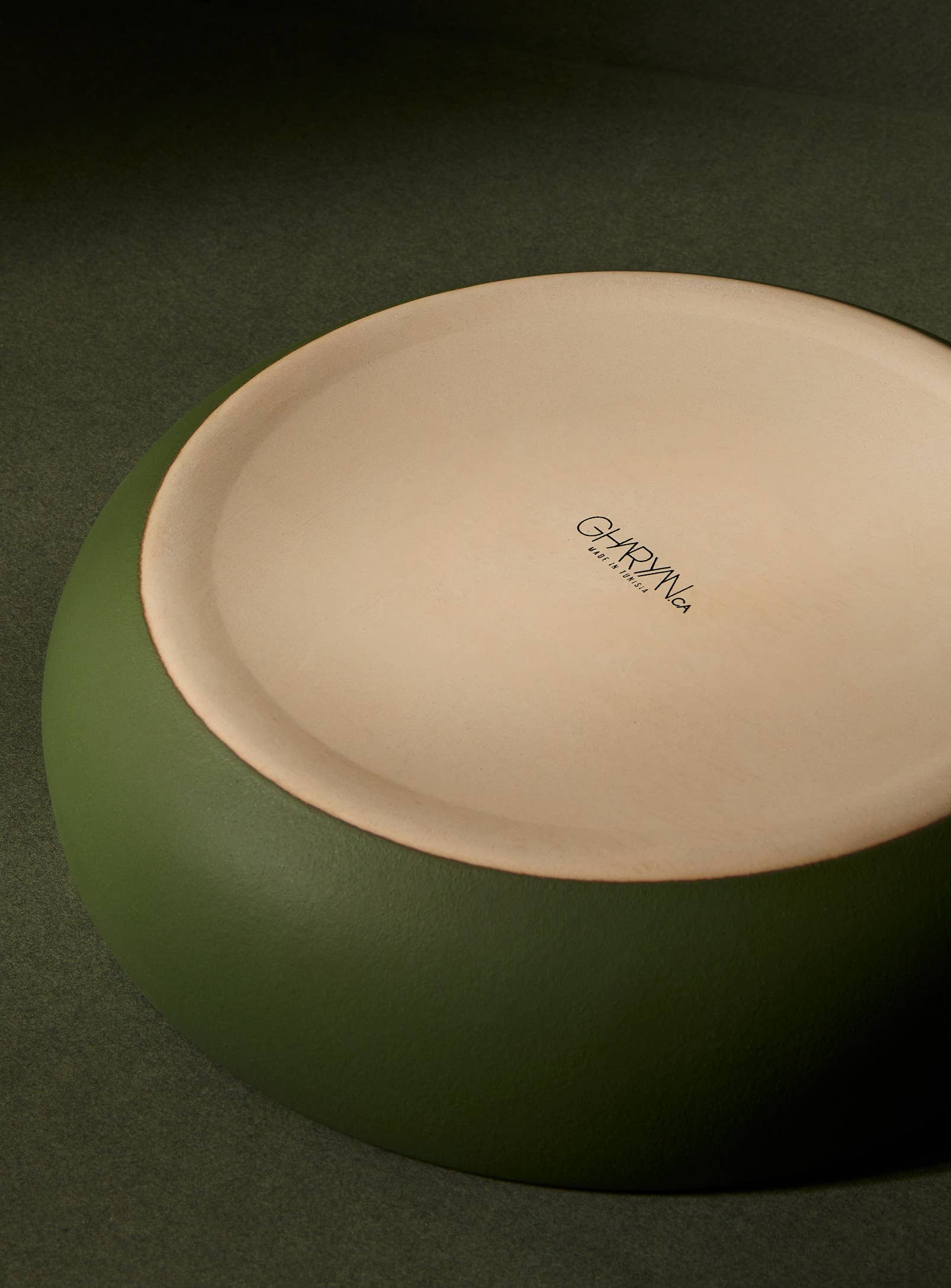 Underside of green ceramic bowl with a visible brand logo on a dark green background
