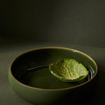 Green ceramic bowl with a leaf on a dark background
