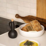 Bowl of bread and a plate of food on a kitchen counter with a black bottle and wooden cutting board.