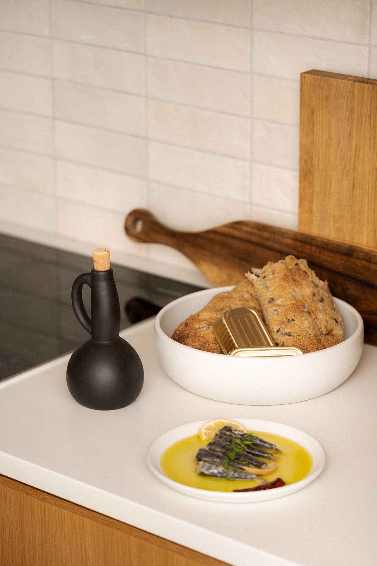 Bowl of bread and a plate of food on a kitchen counter with a black bottle and wooden cutting board.