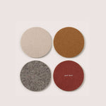 Four round felted wool coasters in beige, brown, gray, and red on a white background.