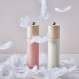 Two salt grinders in white and dark pink with wooden tops on a surface with feathers