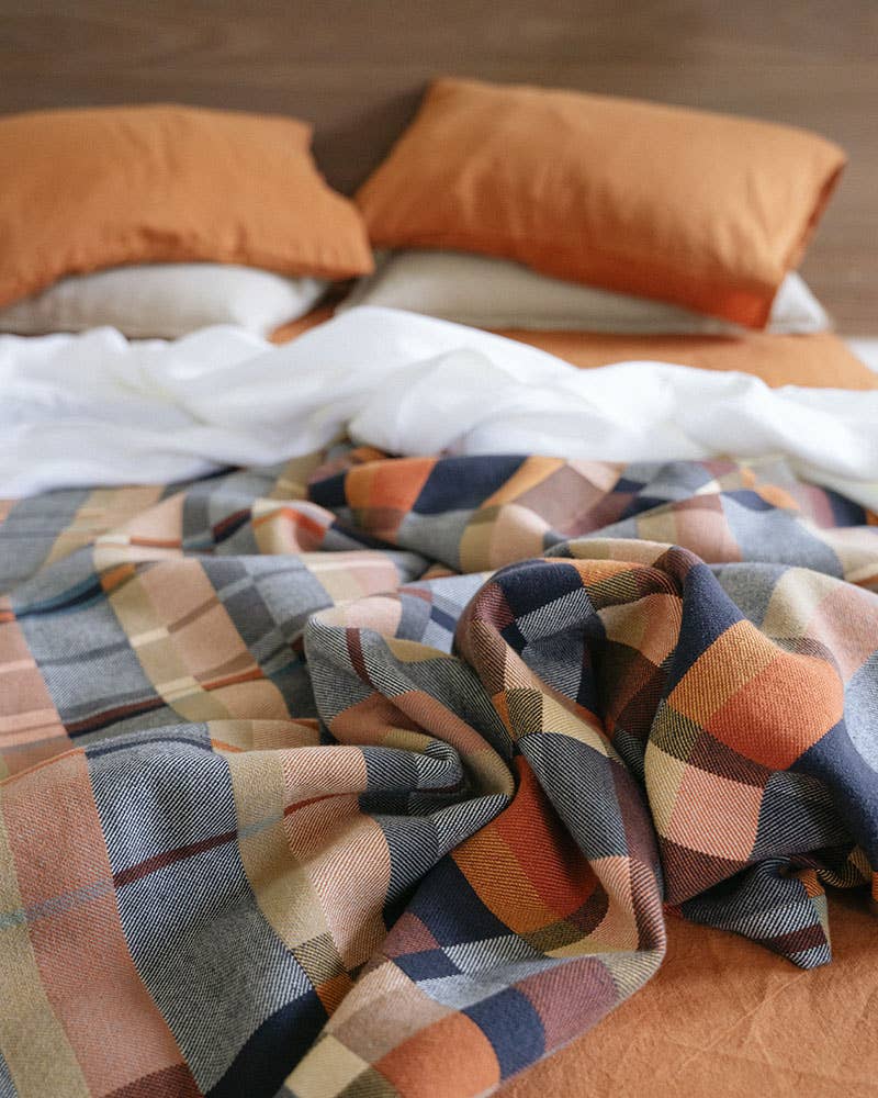 Plaid blanket with autumnal colors on a bed with orange pillows.