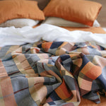 Plaid blanket with autumnal colors on a bed with orange pillows.