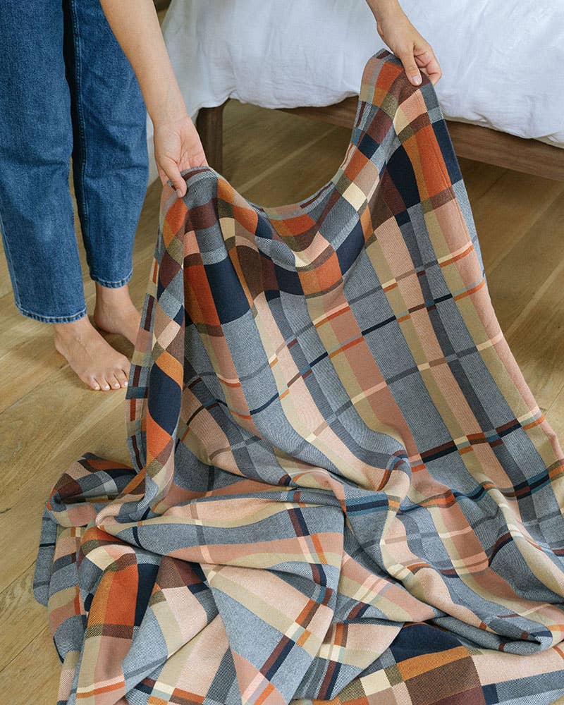 Person holding a plaid blanket on a wooden floor