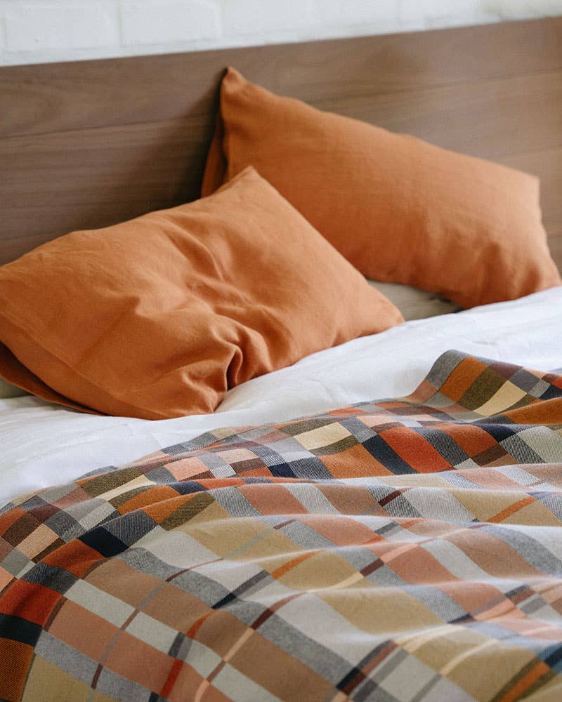 Bed with orange pillows and a plaid blanket on a wooden headboard.