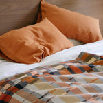 Bed with orange pillows and a plaid blanket on a wooden headboard.