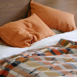 Bed with orange pillows and a plaid blanket on a wooden headboard.