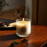 Candle with a logo on a wooden surface, with a cat in the background