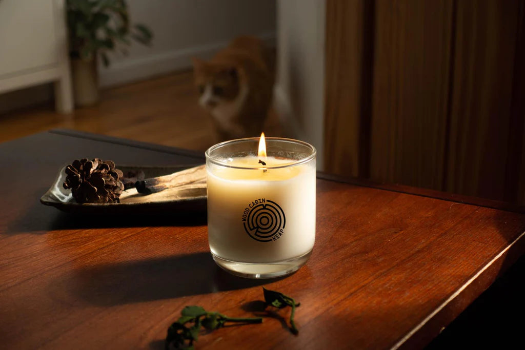 Candle with a logo on a wooden surface, with a cat in the background