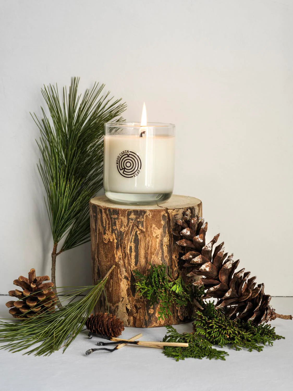 Candle on a wooden stump with pine cones and branches on a light background