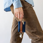 Walking woman holds Marine-colored Merino Wool Card Key Fob on one finger beside her leg in brown pants, white background.
