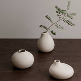Three white ceramic vases on a wooden surface with a minimalistic background