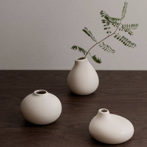 Three white ceramic vases on a wooden surface with a minimalistic background