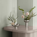 Two silver vases with floral arrangements on a reflective surface.