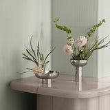 Two silver vases with floral arrangements on a reflective surface.