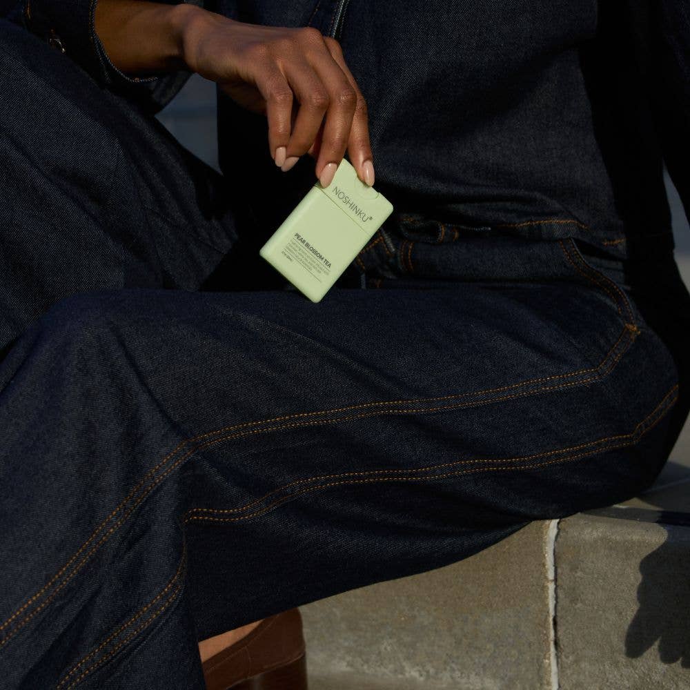 Person holding a green Noshinku sprayer against a dark denim background