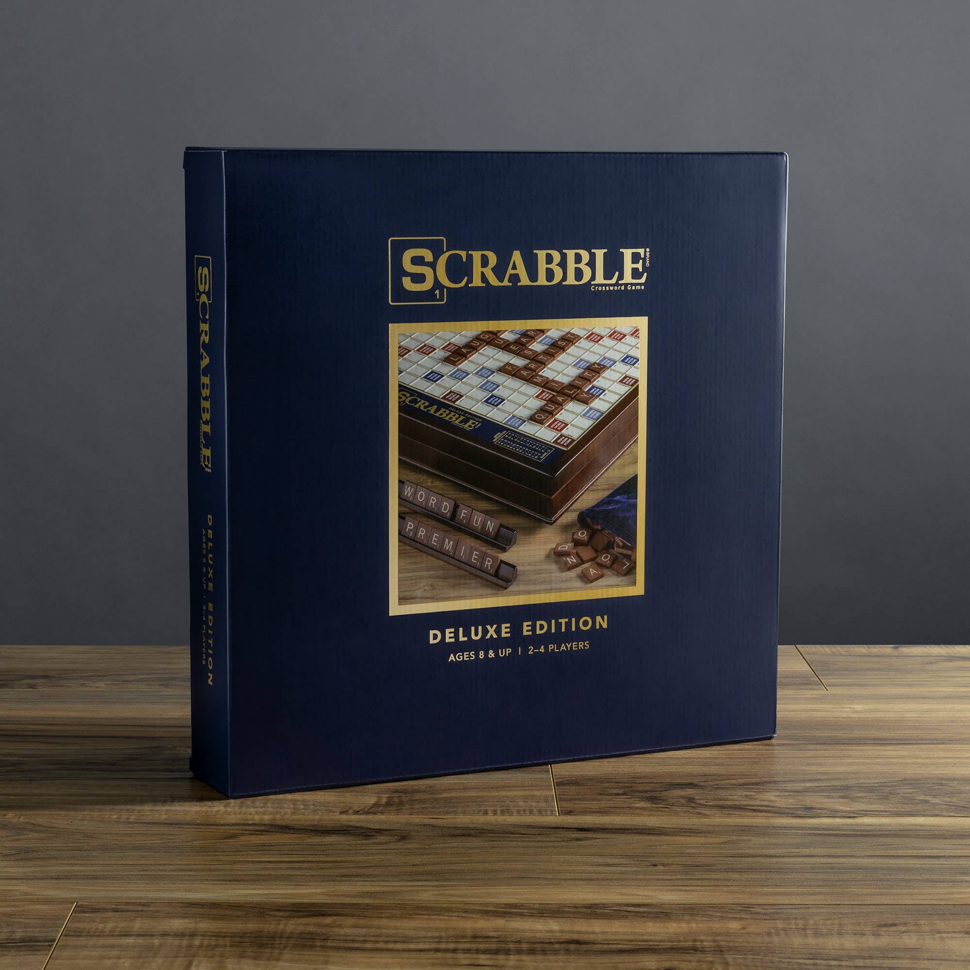 Scrabble Deluxe Edition game box on a wooden surface with a gray background