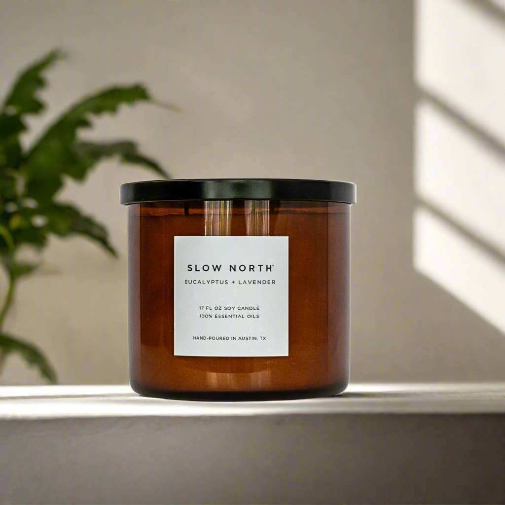 Candle with 'Slow North' label on a surface with a plant in the background