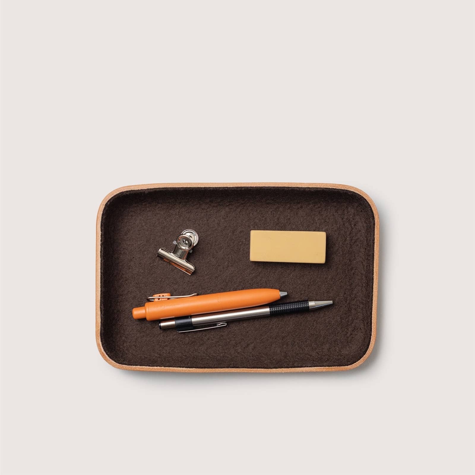 Brown wool and tan leather tray with office supplies including a pen, clip, and business card holder on a light gray background