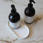 Two black bottles with pump dispensers on a white tray against a marble background