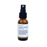 A travel size Slow North linen spray bottle with a label reading 'LINEN SPRAY OF THE SEA'.