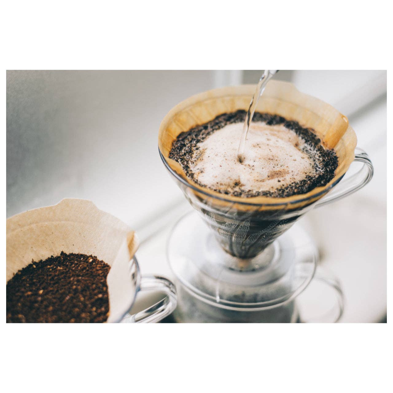 Water being poured into a paper filter and dripper full of coffee grounds on a white background