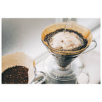 Water being poured into a paper filter and dripper full of coffee grounds on a white background