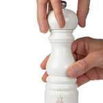White salt mill being held by a hand on a white background