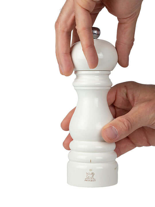 White salt mill being held by a hand on a white background
