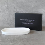 White catchall tray in front of a black Murchison-Hume box on a gray surface
