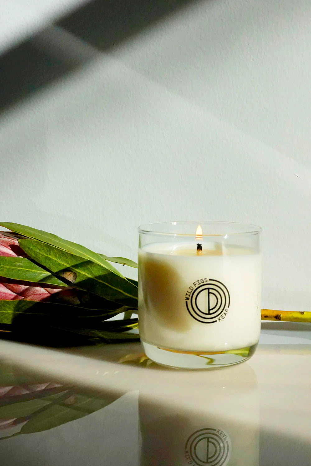 Candle with a logo on a surface next to green leaves