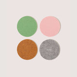 A set of four round wool felt coasters in green, pink, brown, and gray colors, displayed on a white background.