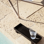 ferm living black xs bon tray with full drinking glass on the ground by chair