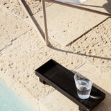 ferm living black xs bon tray with full drinking glass on the ground by chair