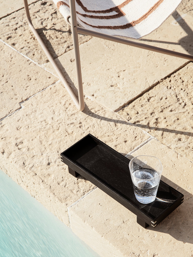 ferm living black xs bon tray with full drinking glass on the ground by chair