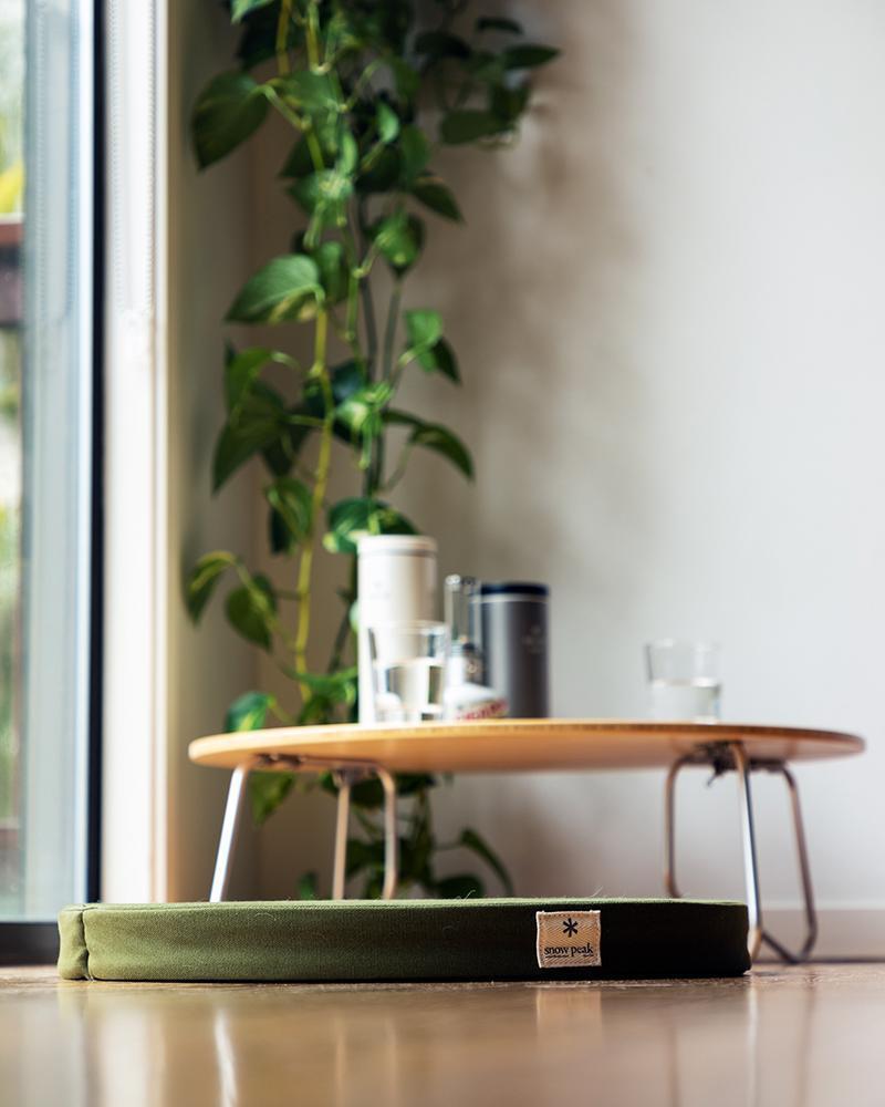 Snow Peak green lounge cushion in the foreground on the floor. A low table with glasses of water and canisters are in the background. 