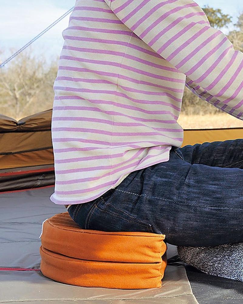 Torso of person in lavendar colored and white striped shirt and jeans sitting on a folded Snow Peak orange cushion. 