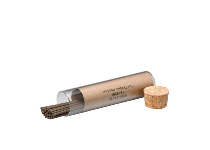 Incense sticks in a cylindrical glass holder with cork lid on a white background