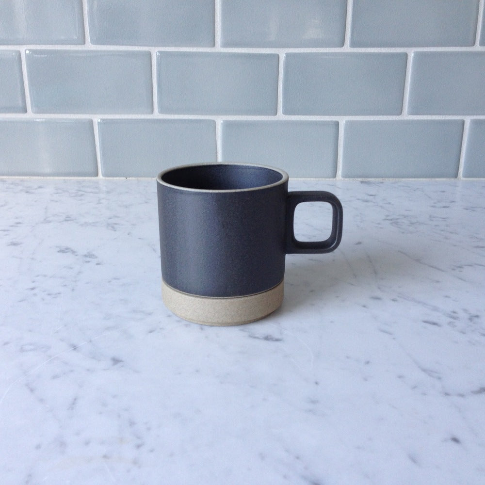 Hasami Porcelain 11 oz black mug resting on the natural coaster, sitting on a white marble counter top with a grey tile backsplash.