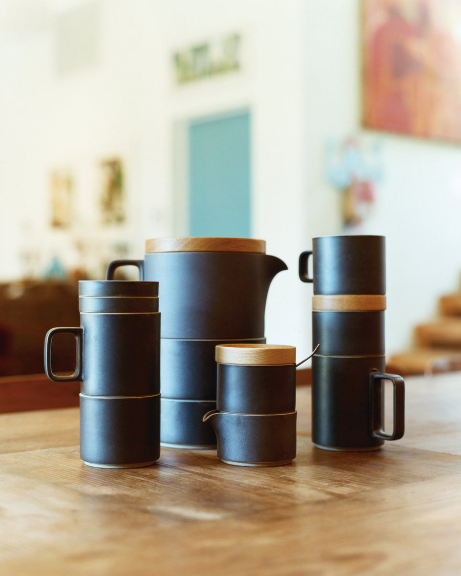Black Hasami Porcleain teapot, mugs and creamer and sugar pot on a table.