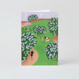 A greeting card depicting a hand-painted scene with lilac bushes and a sky of the same color, with people in a park pathway.