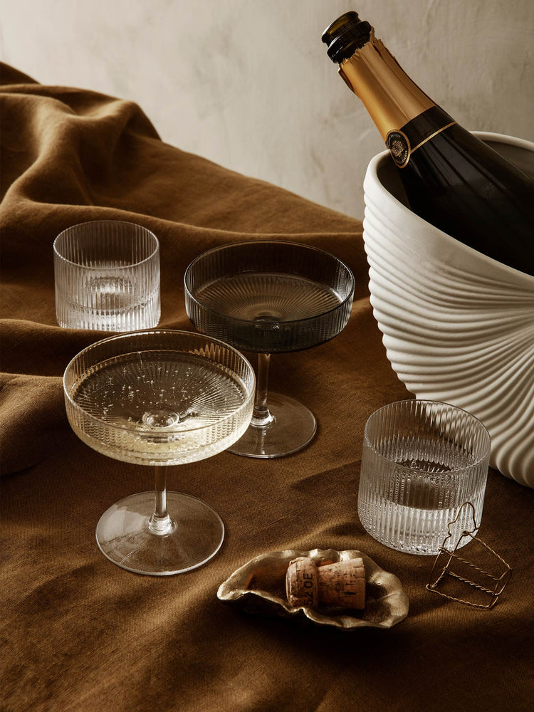 glass champagne coupes and low tumblers on brown velvet tablecloth next to bottle of champagne